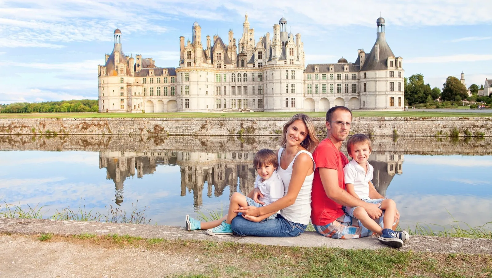 A family sitting by the water with Château de Chambord behind them