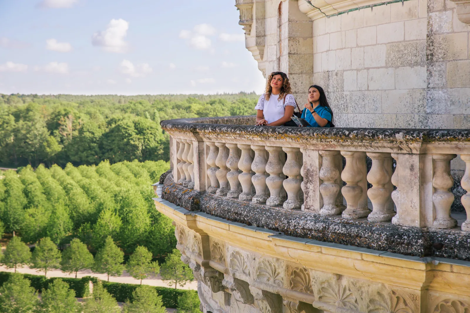 Visitors on a Chambord balcony looking out over the clipped lime avenues