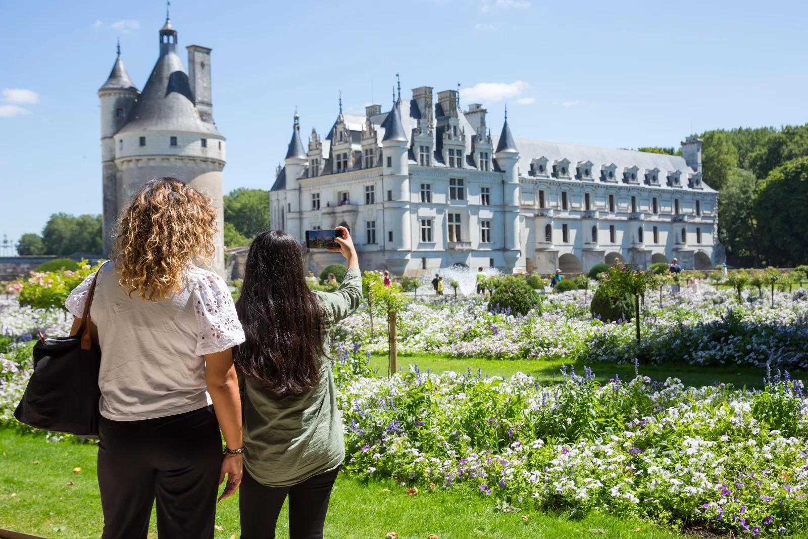 Two visitors photographing Château de Chenonceau from its flower garden