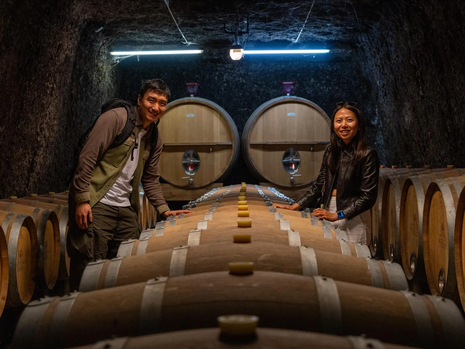 Two guests between rows of oak barrels in a tufa-stone Loire wine cellar