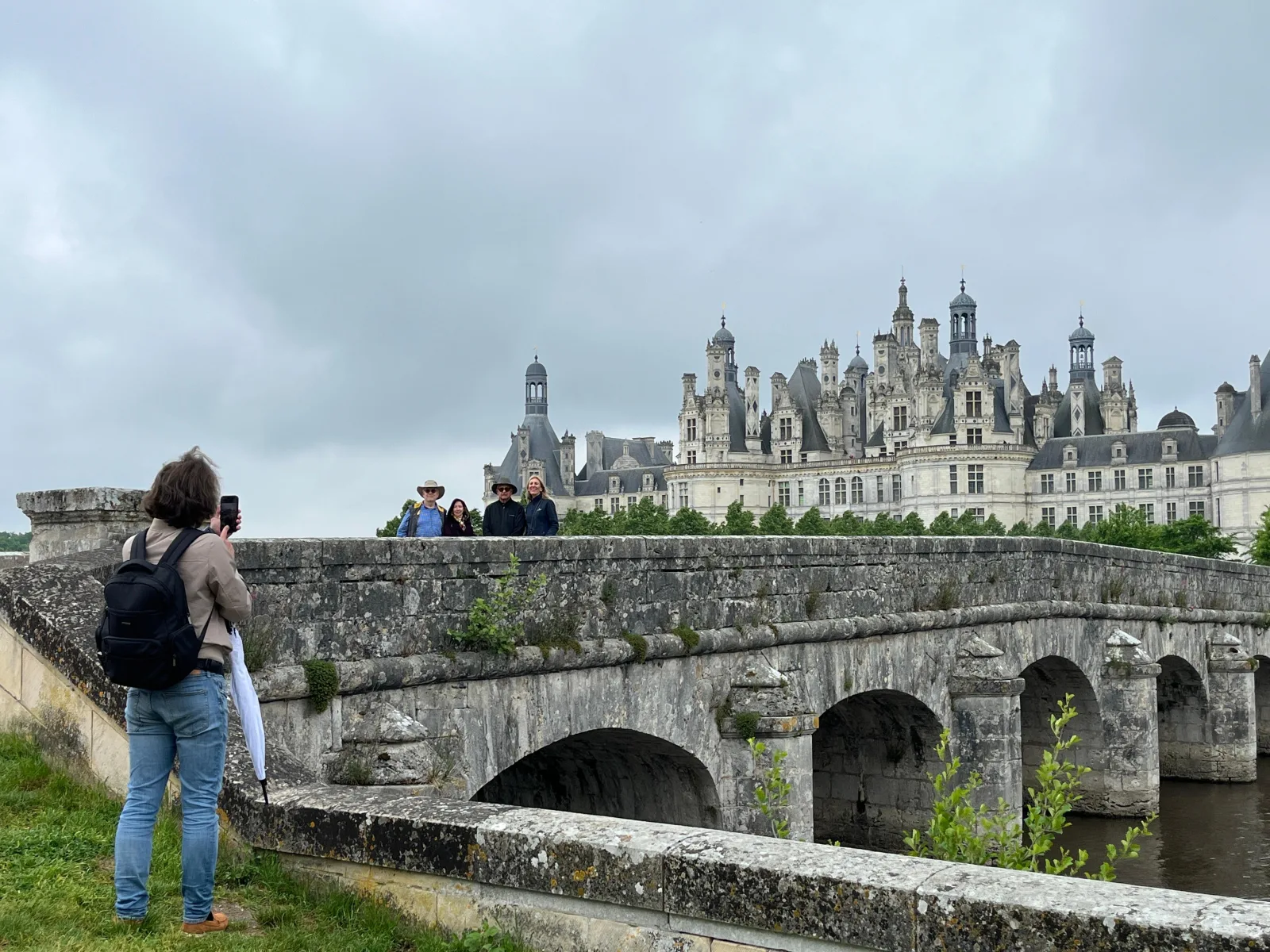 A visitor photographing Chambord from the old stone bridge over the Cosson