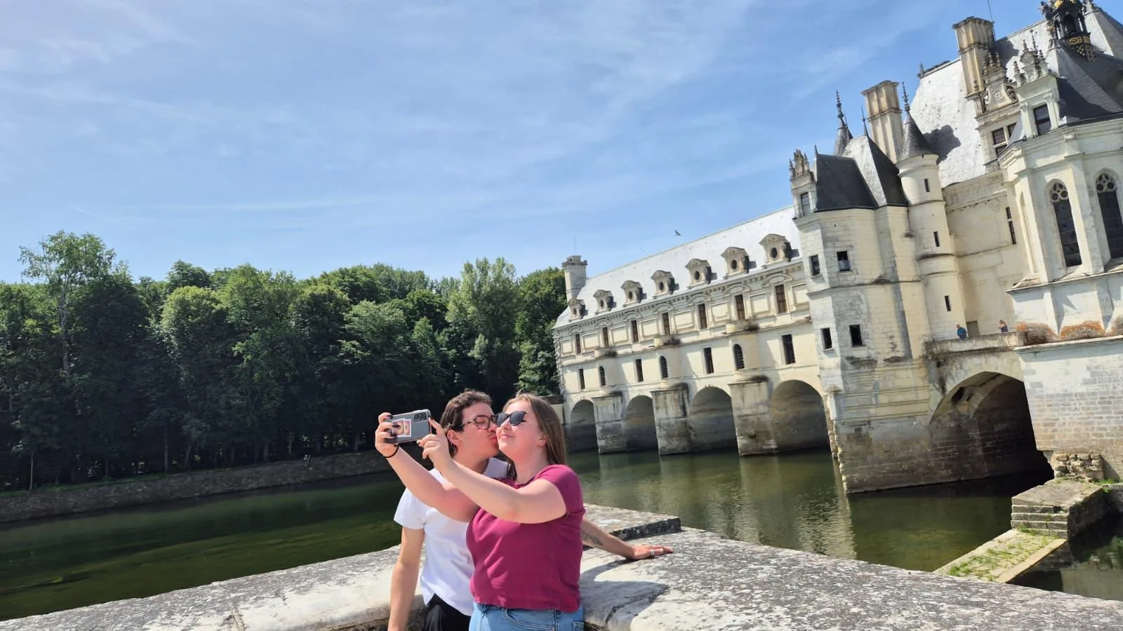 Two travellers photographing Chenonceau's gallery from the riverside wall