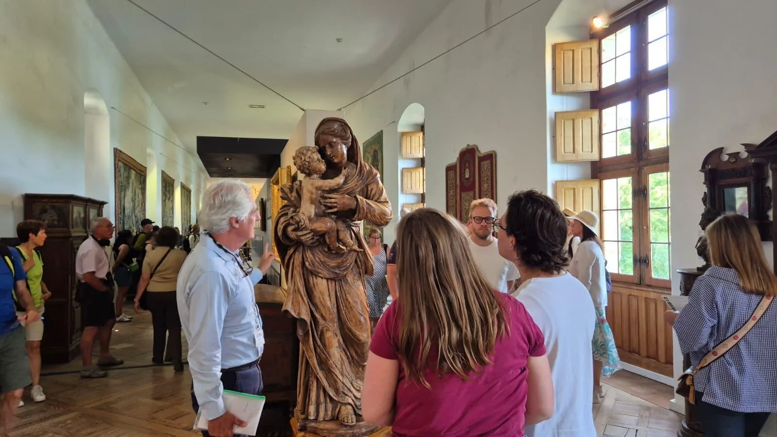 A group in Cheverny's furnished gallery beside a carved wooden statue